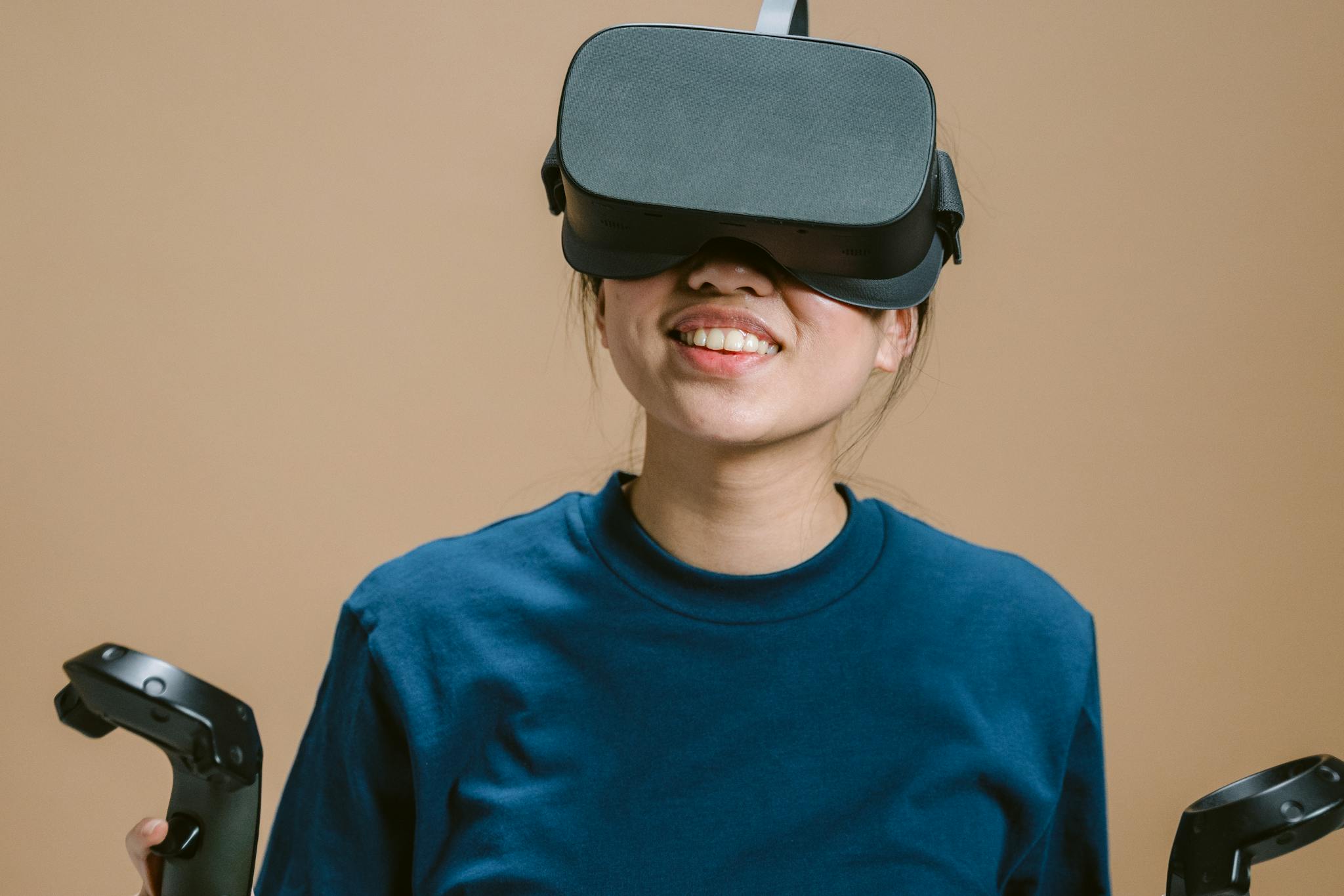 Smiling teenage girl using VR headset and controllers indoors.
